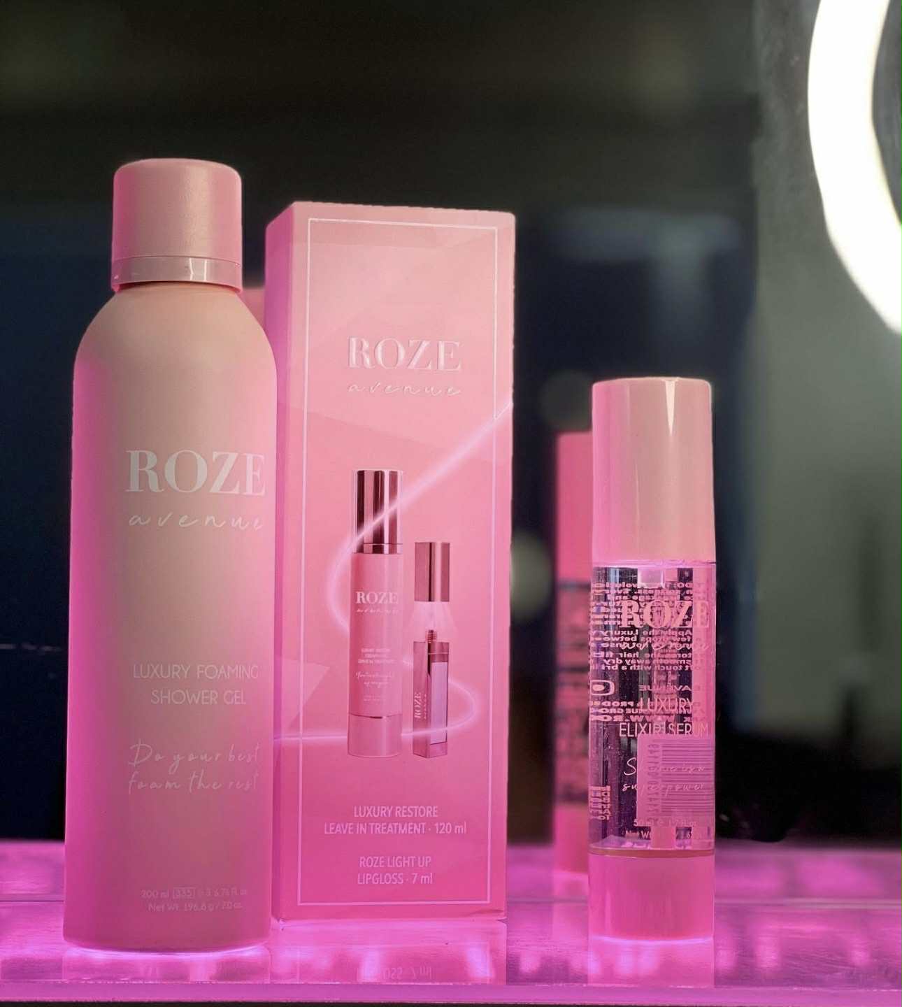 Produkter fra Boze i lyserød indpakning, som står på et bord der lyser det op i pink.